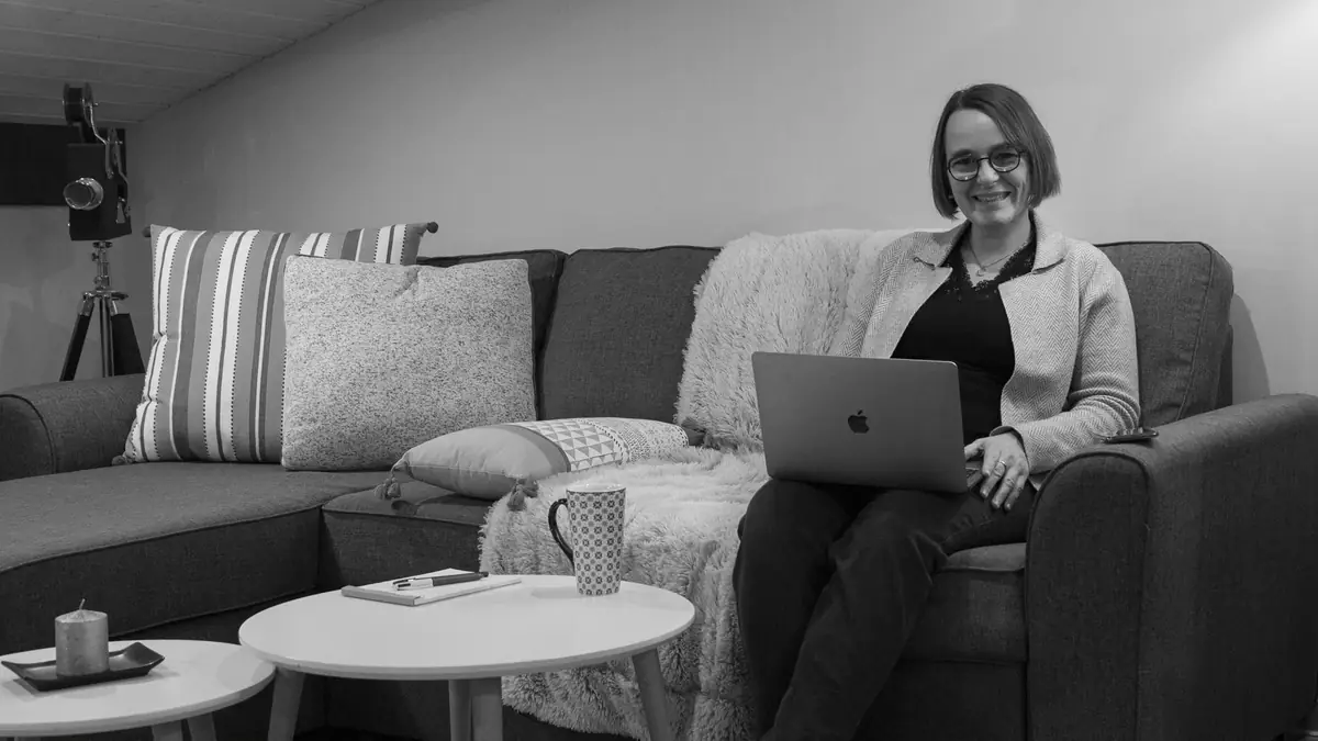 Coralie, souriante, son ordinateur sur les genoux dans son agence